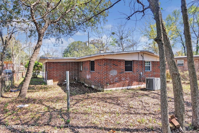 view of property exterior with central air condition unit, fence, and brick siding