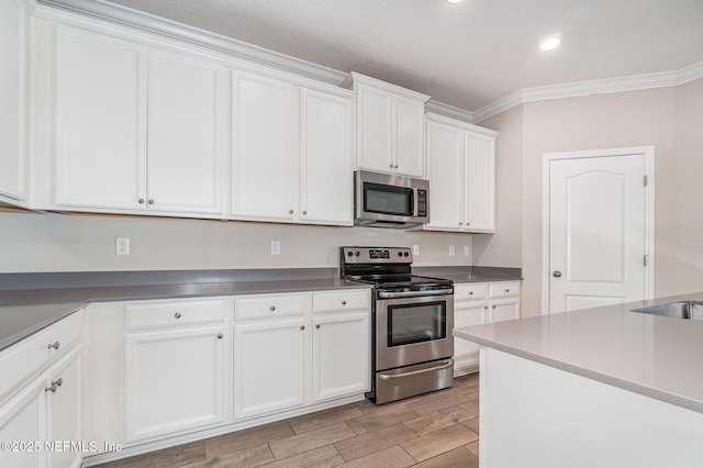 kitchen featuring wood finish floors, ornamental molding, recessed lighting, stainless steel appliances, and white cabinets