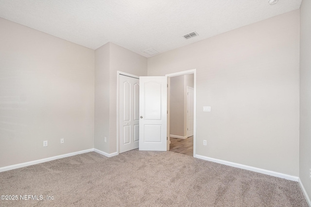 unfurnished bedroom featuring visible vents, a textured ceiling, a closet, carpet floors, and baseboards