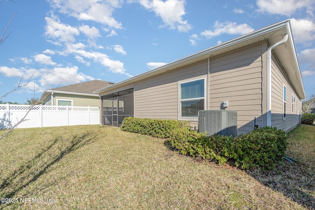 rear view of property with central AC unit, a lawn, fence, and a sunroom