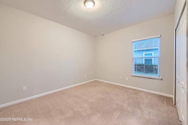unfurnished room with light colored carpet, baseboards, and a textured ceiling