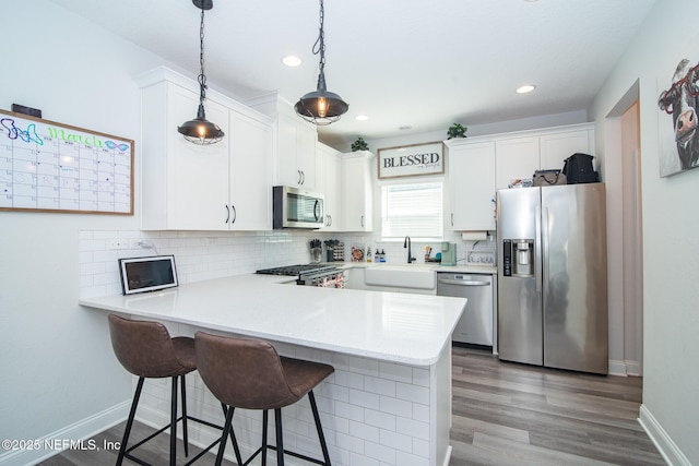 kitchen with backsplash, light countertops, a peninsula, stainless steel appliances, and a sink