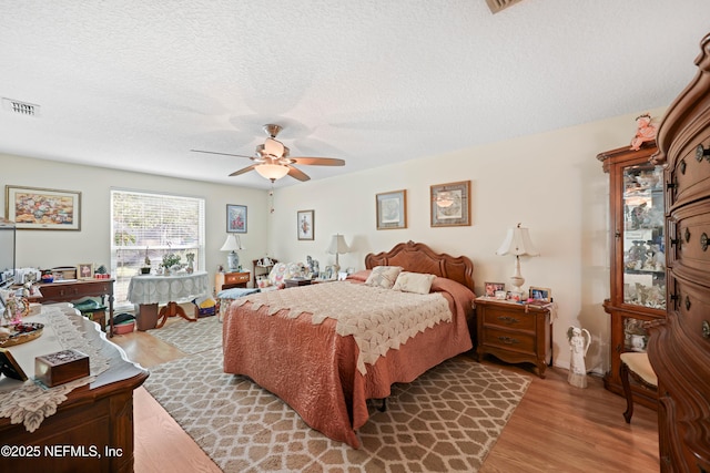 bedroom featuring a textured ceiling, visible vents, light wood finished floors, and ceiling fan