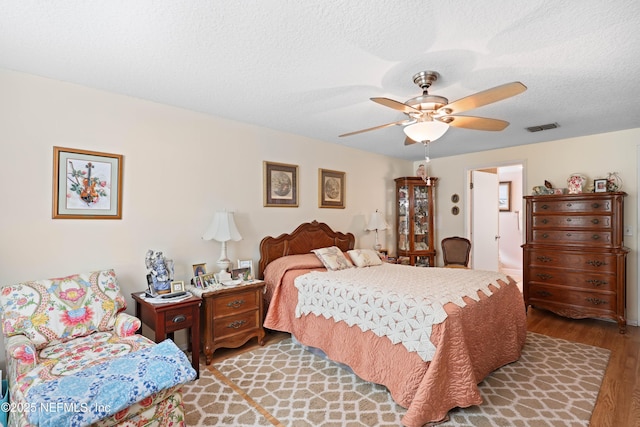 bedroom featuring light wood finished floors, visible vents, a textured ceiling, and a ceiling fan