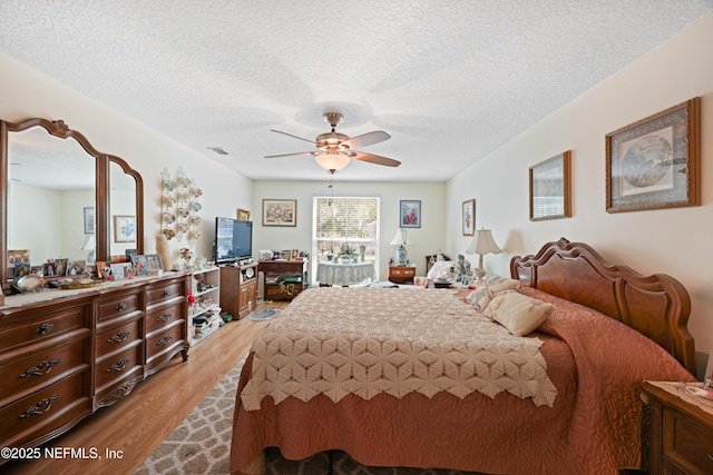 bedroom featuring a textured ceiling, visible vents, light wood finished floors, and ceiling fan