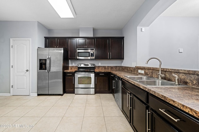 kitchen featuring dark brown cabinetry, light tile patterned floors, appliances with stainless steel finishes, and a sink