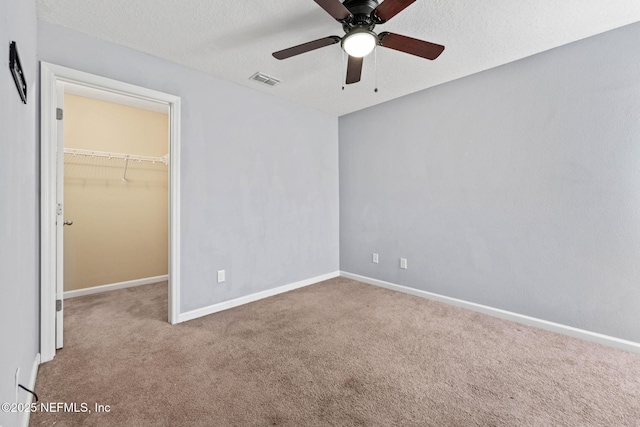 unfurnished bedroom featuring visible vents, a walk in closet, baseboards, carpet, and a textured ceiling