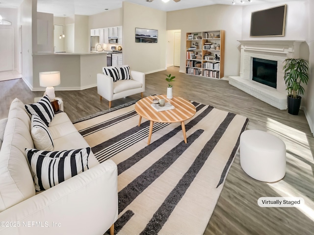 living area with wood finished floors, a fireplace with raised hearth, and baseboards