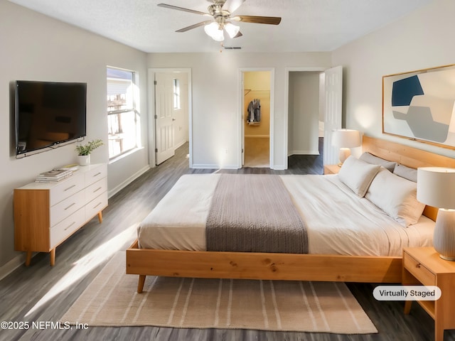 bedroom with visible vents, a walk in closet, baseboards, ensuite bathroom, and wood finished floors