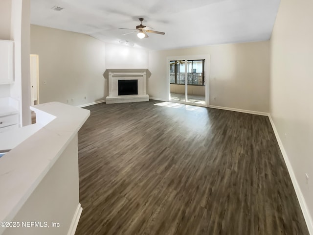 unfurnished living room with baseboards, dark wood finished floors, lofted ceiling, a fireplace, and ceiling fan