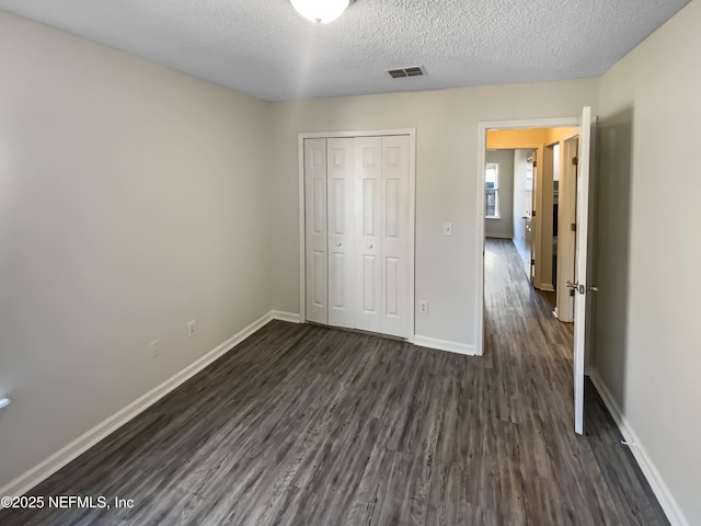 unfurnished bedroom featuring visible vents, baseboards, a closet, a textured ceiling, and dark wood-style flooring