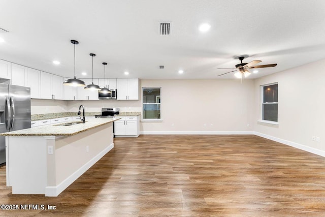 kitchen with a center island with sink, light wood finished floors, a sink, white cabinets, and appliances with stainless steel finishes