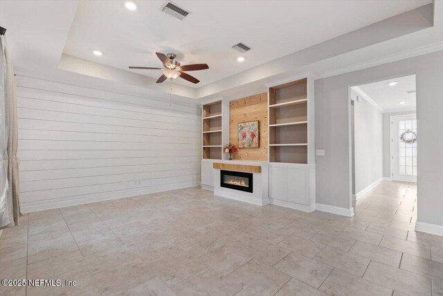 unfurnished living room featuring a glass covered fireplace, a tray ceiling, built in features, and visible vents