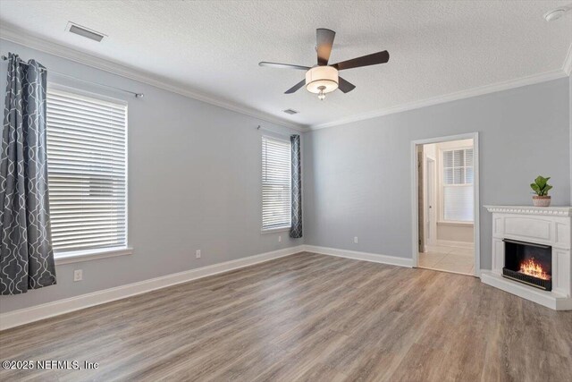 unfurnished living room featuring visible vents, crown molding, light wood-style flooring, a warm lit fireplace, and a textured ceiling