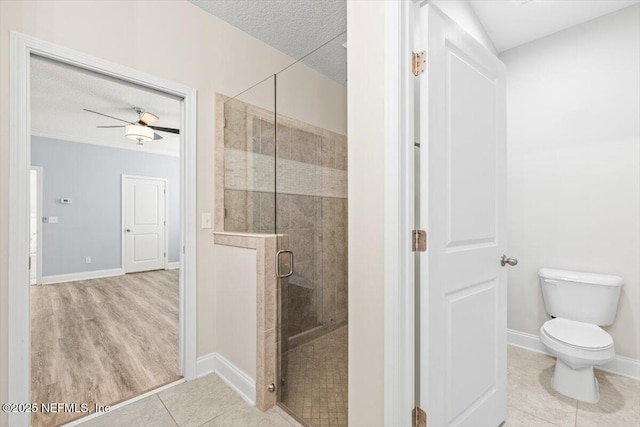 bathroom with tile patterned flooring, toilet, a stall shower, a textured ceiling, and a ceiling fan