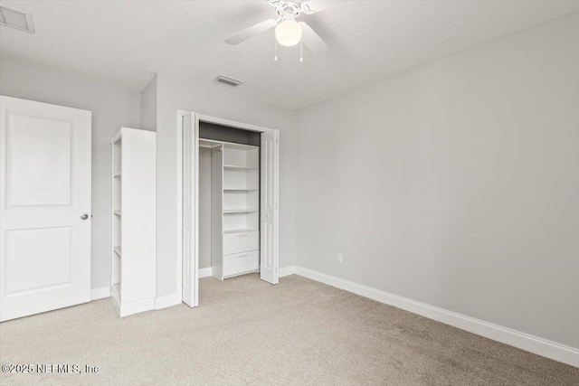 unfurnished bedroom featuring visible vents, light carpet, a textured ceiling, a closet, and baseboards