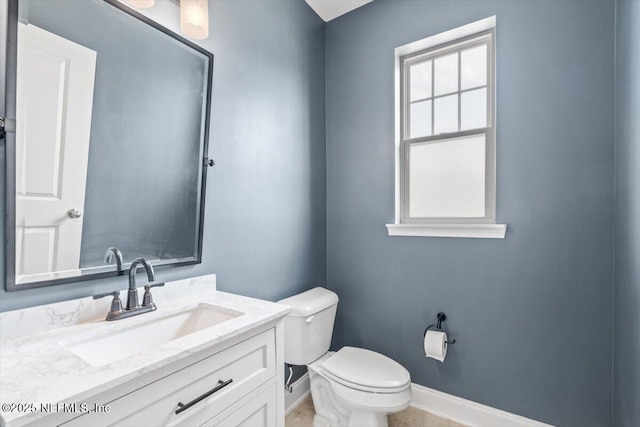 half bathroom featuring toilet, vanity, and baseboards