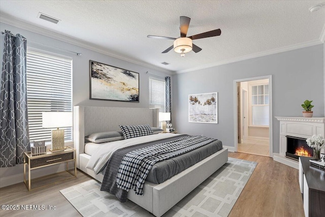 bedroom featuring visible vents, a warm lit fireplace, light wood-style flooring, and crown molding