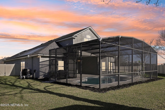 back of house featuring glass enclosure, fence, a lawn, and stucco siding