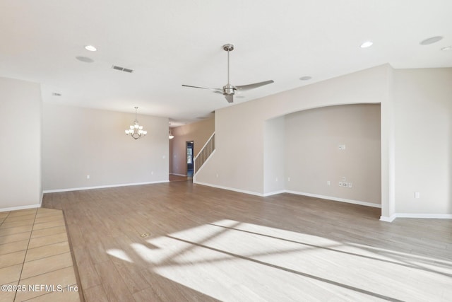 unfurnished living room featuring wood finished floors, visible vents, recessed lighting, stairs, and ceiling fan with notable chandelier