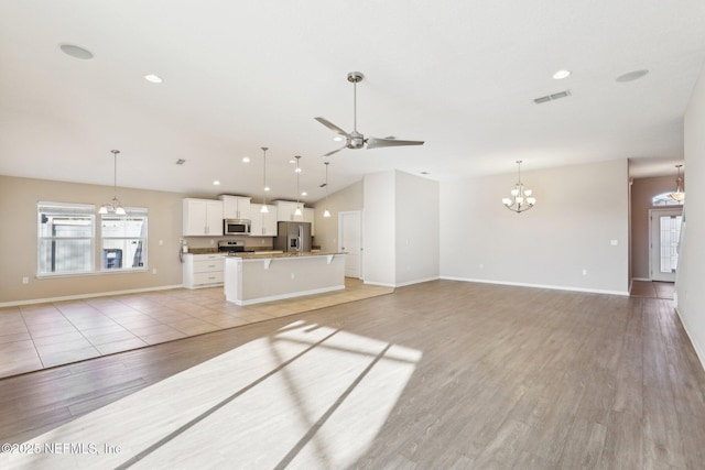 unfurnished living room with vaulted ceiling, plenty of natural light, ceiling fan with notable chandelier, and visible vents