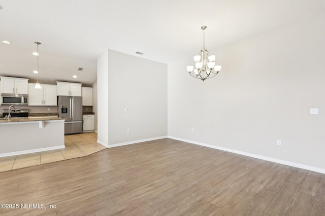 interior space with a notable chandelier, appliances with stainless steel finishes, light wood-style floors, and a sink