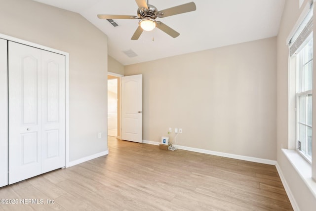 unfurnished bedroom with visible vents, light wood-style flooring, a closet, baseboards, and vaulted ceiling