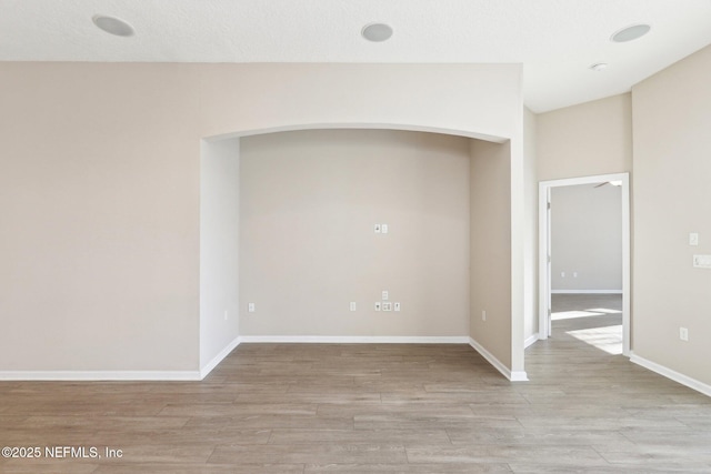 unfurnished room featuring arched walkways, light wood-style flooring, and baseboards