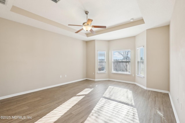 spare room with ceiling fan, baseboards, a raised ceiling, and wood finished floors