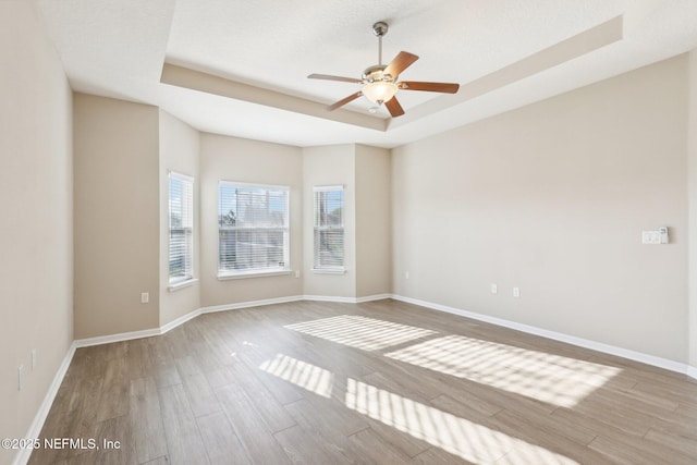 empty room featuring ceiling fan, a tray ceiling, baseboards, and wood finished floors