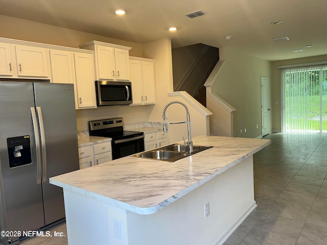 kitchen with visible vents, an island with sink, a sink, stainless steel appliances, and white cabinets