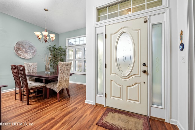 entrance foyer featuring wood finished floors, baseboards, lofted ceiling, a textured ceiling, and a chandelier