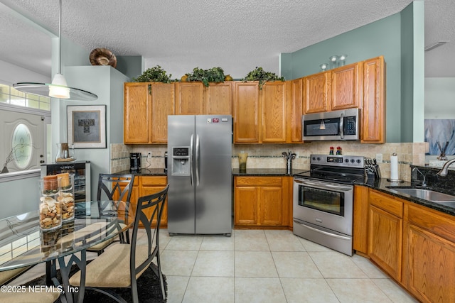 kitchen featuring light tile patterned flooring, stainless steel appliances, brown cabinetry, and a sink