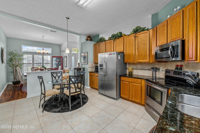 kitchen with decorative backsplash, brown cabinets, an inviting chandelier, light tile patterned flooring, and stainless steel appliances