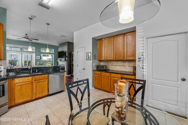 kitchen with ceiling fan, light tile patterned floors, brown cabinets, appliances with stainless steel finishes, and a sink