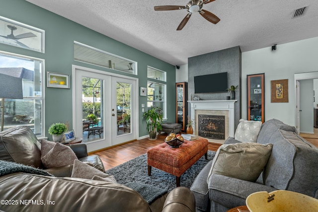 living area featuring visible vents, ceiling fan, a fireplace, wood finished floors, and a textured ceiling