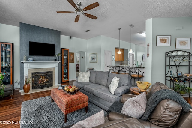 living area featuring a textured ceiling, a lit fireplace, wood finished floors, and a ceiling fan