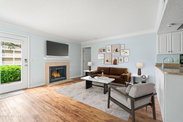 living room featuring crown molding, baseboards, a tile fireplace, light wood-style floors, and a textured ceiling