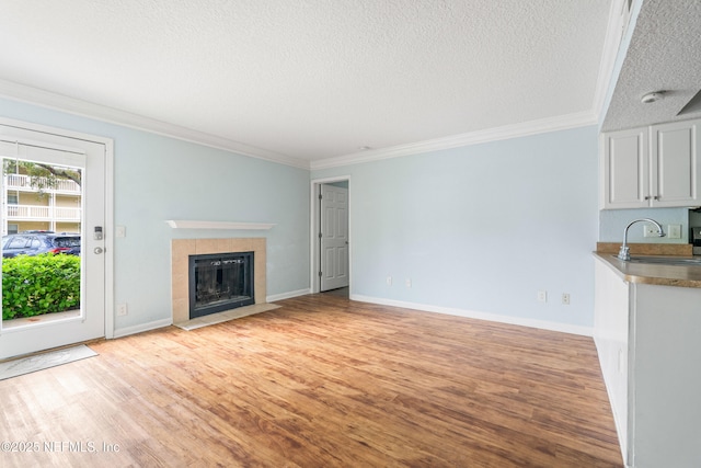 unfurnished living room with ornamental molding, a sink, a textured ceiling, light wood-style floors, and a fireplace