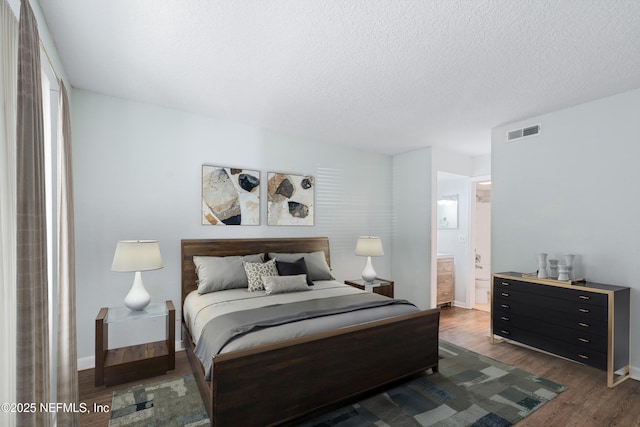 bedroom with visible vents, ensuite bathroom, a textured ceiling, wood finished floors, and baseboards