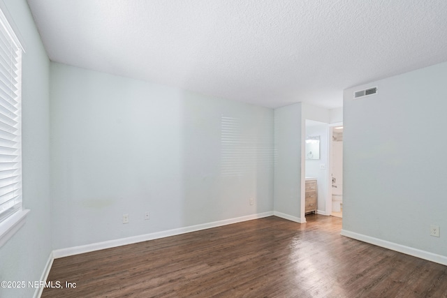 unfurnished room featuring dark wood finished floors, baseboards, visible vents, and a textured ceiling