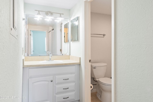 bathroom featuring vanity, toilet, a textured wall, and tile patterned flooring