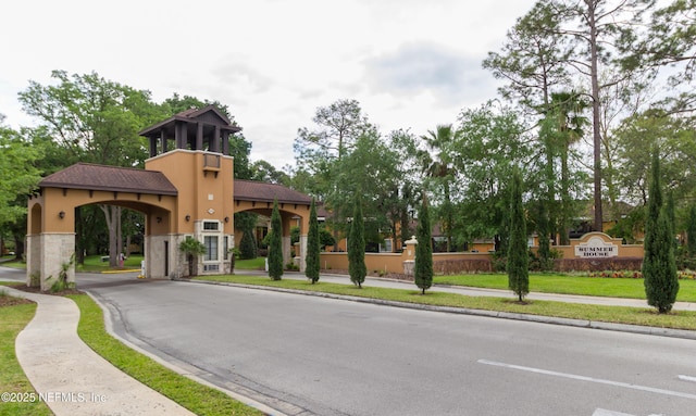 view of road featuring sidewalks, curbs, and a gated entry