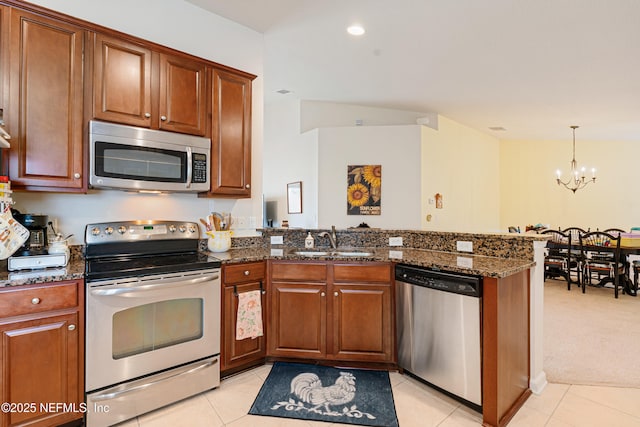 kitchen featuring dark stone counters, light tile patterned floors, appliances with stainless steel finishes, a peninsula, and a sink