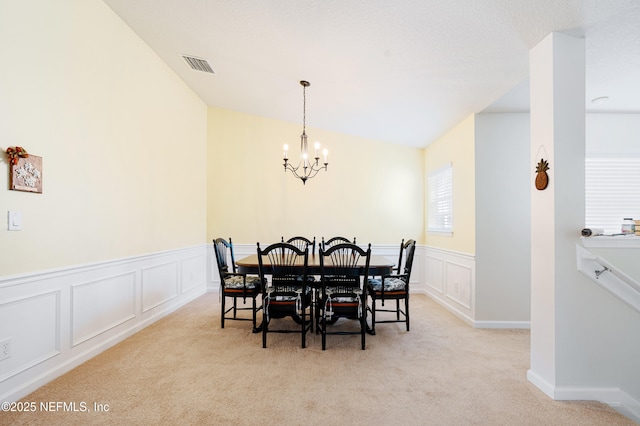 dining area with a chandelier, visible vents, a decorative wall, and carpet