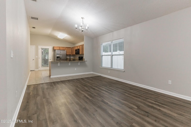 unfurnished living room featuring visible vents, baseboards, dark wood finished floors, a chandelier, and vaulted ceiling