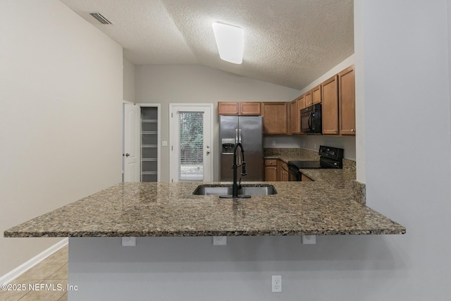 kitchen featuring visible vents, brown cabinets, a peninsula, black appliances, and a sink