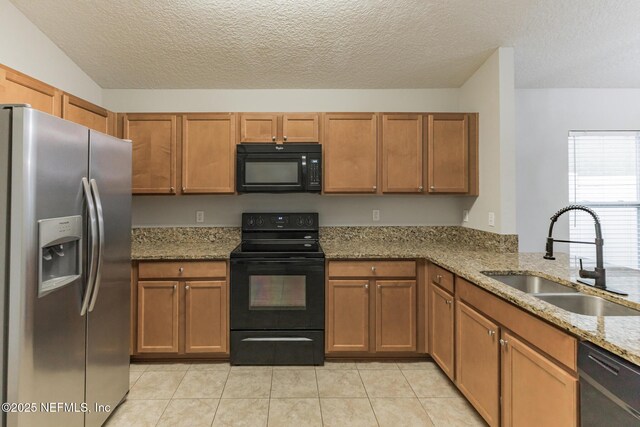 kitchen with light stone countertops, brown cabinets, light tile patterned flooring, black appliances, and a sink