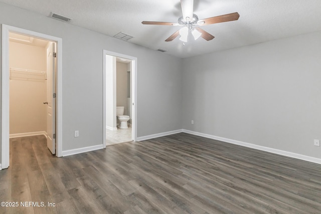 unfurnished bedroom featuring a walk in closet, dark wood-type flooring, baseboards, and visible vents