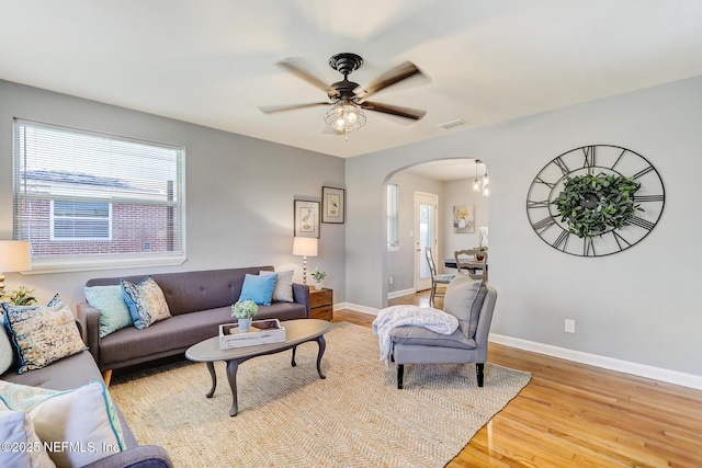 living room featuring visible vents, baseboards, ceiling fan, wood finished floors, and arched walkways